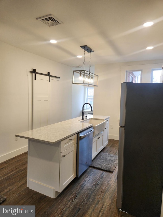 kitchen featuring a barn door, decorative light fixtures, a kitchen island with sink, white cabinets, and appliances with stainless steel finishes