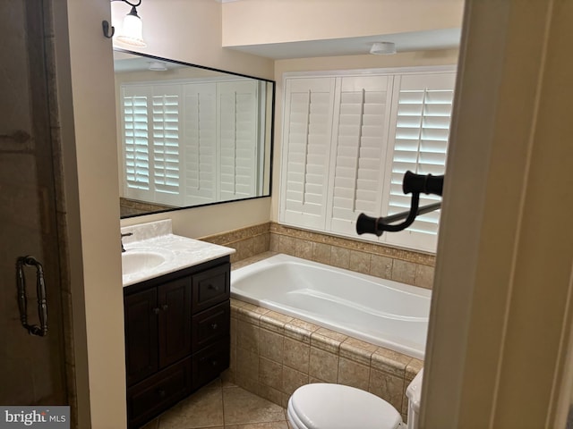 bathroom with tile patterned floors, vanity, a relaxing tiled tub, and toilet