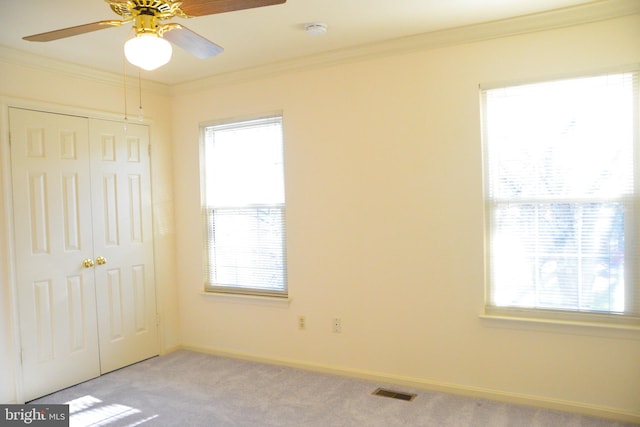 unfurnished bedroom featuring ceiling fan, a closet, light colored carpet, and ornamental molding