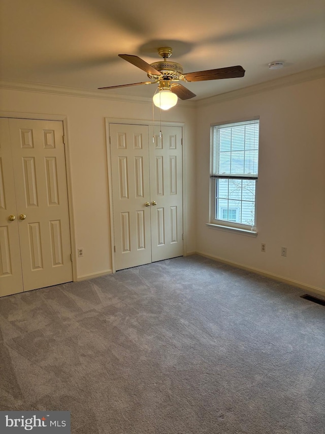 unfurnished bedroom with ceiling fan, light colored carpet, two closets, and ornamental molding