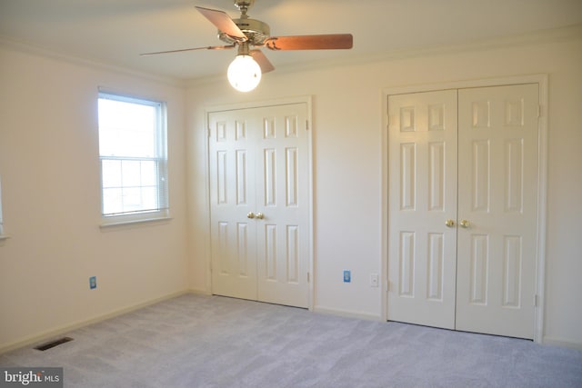 unfurnished bedroom with ceiling fan, light colored carpet, ornamental molding, and multiple closets