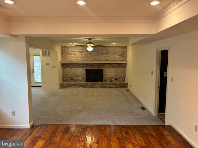 unfurnished living room with ceiling fan, brick wall, dark hardwood / wood-style floors, crown molding, and a fireplace