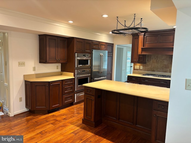 kitchen featuring crown molding, appliances with stainless steel finishes, tasteful backsplash, dark hardwood / wood-style flooring, and a chandelier