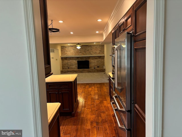 kitchen featuring dark hardwood / wood-style flooring, a brick fireplace, brick wall, ceiling fan, and crown molding