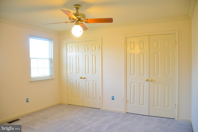 unfurnished bedroom featuring multiple closets, ceiling fan, light colored carpet, and ornamental molding