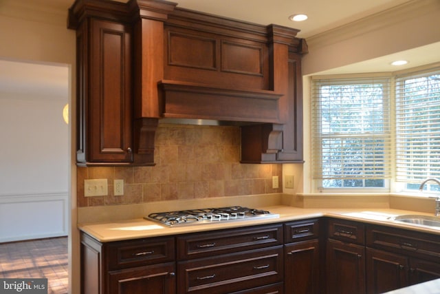 kitchen with sink, decorative backsplash, ornamental molding, custom range hood, and stainless steel gas cooktop