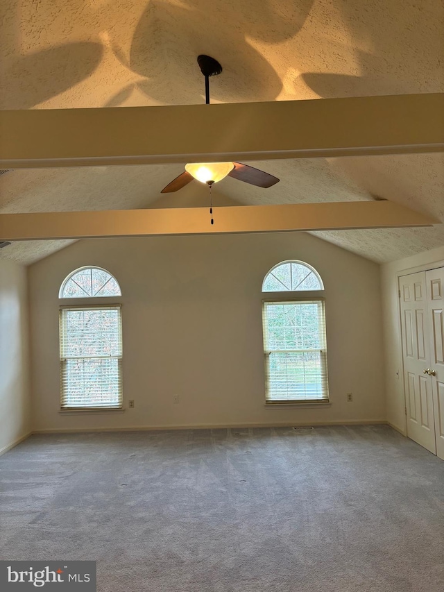 carpeted empty room with vaulted ceiling with beams, a wealth of natural light, ceiling fan, and a textured ceiling