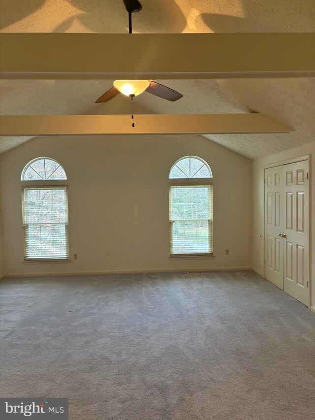 carpeted spare room with vaulted ceiling with beams, a wealth of natural light, ceiling fan, and a textured ceiling