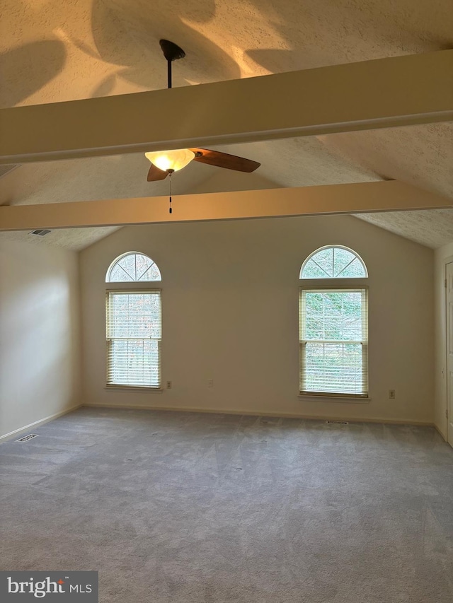 spare room with a textured ceiling, vaulted ceiling with beams, carpet floors, and a healthy amount of sunlight