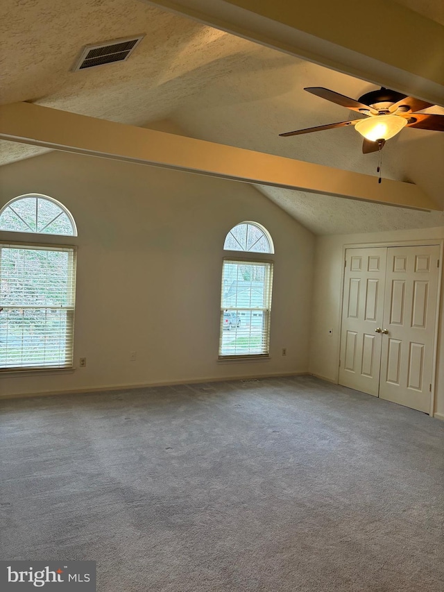 carpeted spare room featuring lofted ceiling with beams, ceiling fan, and a textured ceiling