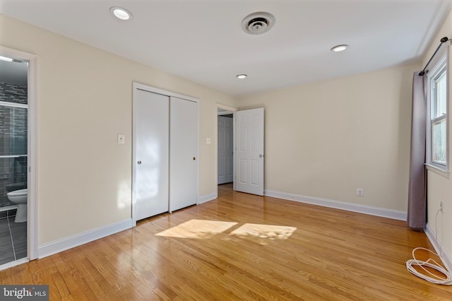 unfurnished bedroom with ensuite bath, a closet, and light hardwood / wood-style flooring