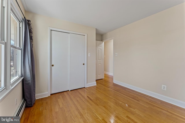 unfurnished bedroom featuring a closet, baseboard heating, and light hardwood / wood-style flooring