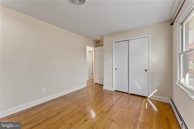 unfurnished bedroom with a closet, light wood-type flooring, and a baseboard heating unit