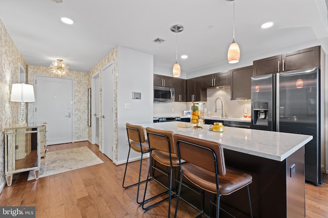 kitchen featuring dark brown cabinets, light wood-type flooring, stainless steel appliances, and a breakfast bar