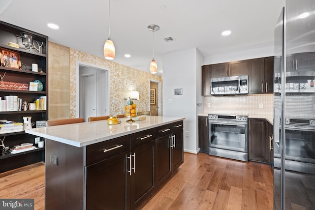 kitchen featuring a center island, hanging light fixtures, dark brown cabinets, appliances with stainless steel finishes, and light wood-type flooring