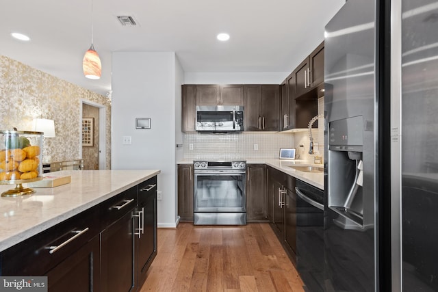 kitchen featuring sink, hanging light fixtures, light stone counters, light hardwood / wood-style floors, and appliances with stainless steel finishes