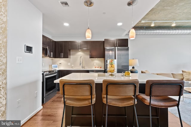 kitchen with a center island, a kitchen breakfast bar, light hardwood / wood-style flooring, decorative light fixtures, and stainless steel appliances