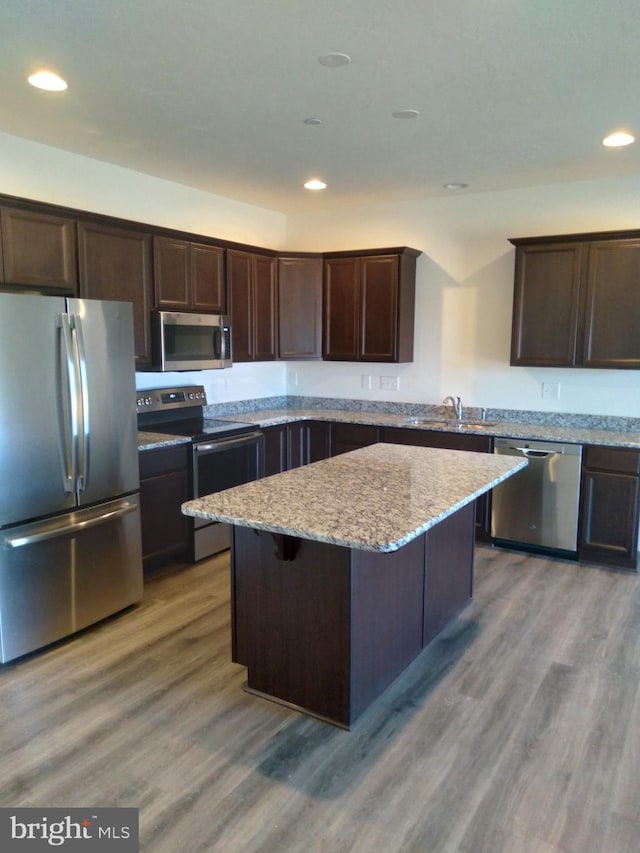 kitchen with dark brown cabinetry, light stone countertops, stainless steel appliances, and hardwood / wood-style flooring