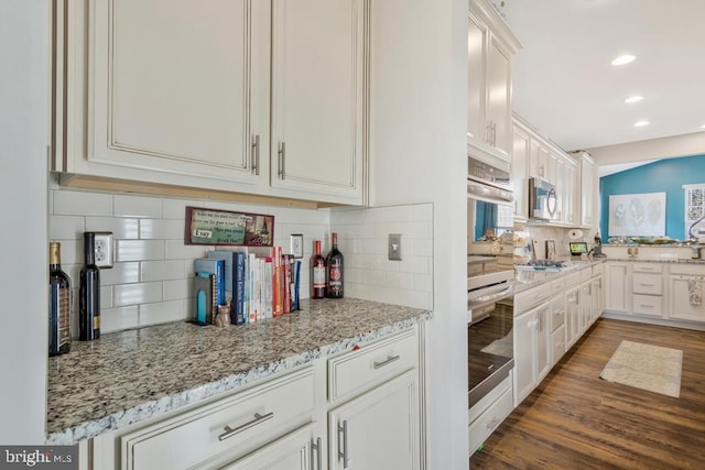 kitchen featuring appliances with stainless steel finishes, light stone countertops, white cabinets, dark hardwood / wood-style flooring, and decorative backsplash