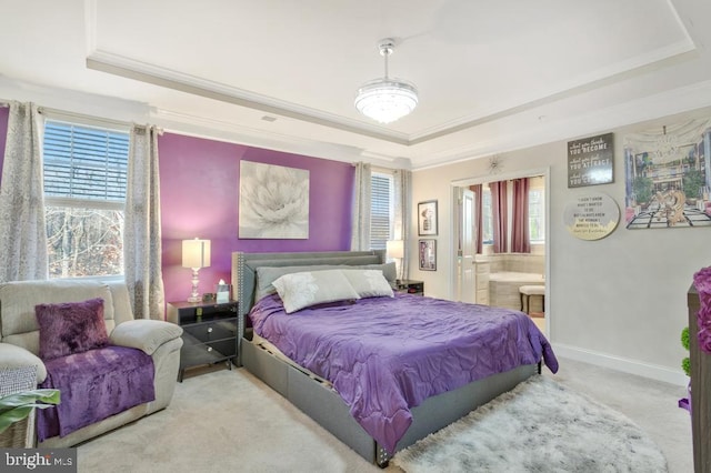 bedroom with multiple windows, connected bathroom, a tray ceiling, and light colored carpet