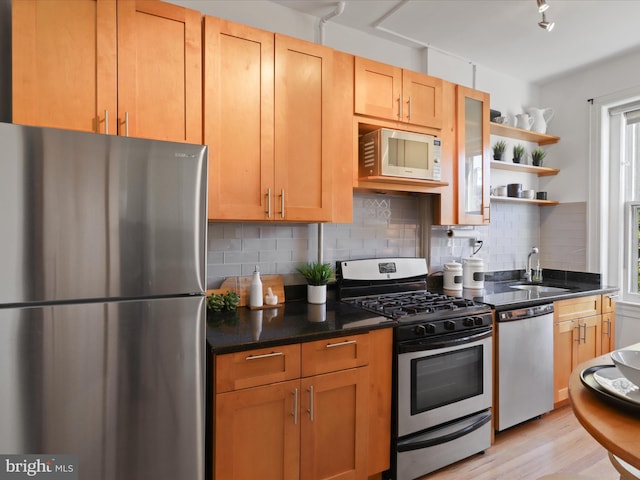 kitchen with sink, tasteful backsplash, track lighting, appliances with stainless steel finishes, and light hardwood / wood-style floors