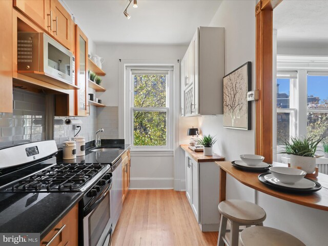 kitchen with sink, dark stone countertops, stainless steel appliances, light hardwood / wood-style floors, and backsplash