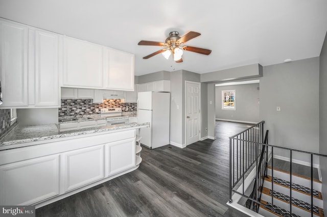 kitchen with dark wood-type flooring, white refrigerator, range with electric stovetop, light stone counters, and white cabinetry