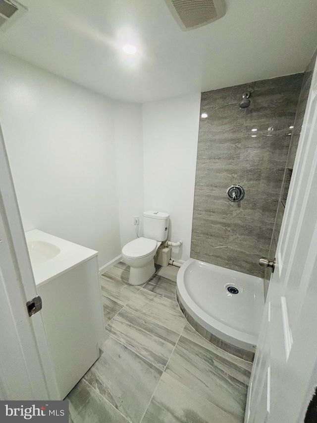 bathroom with a tile shower, vanity, and toilet