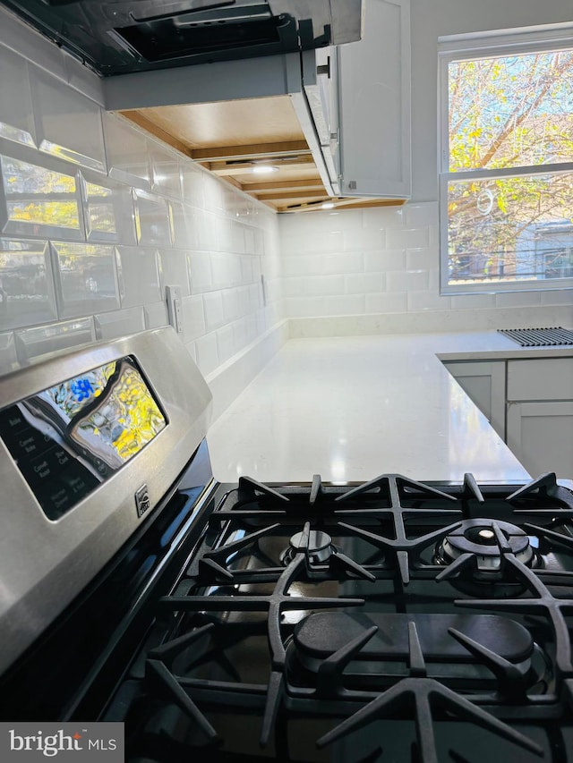 room details featuring decorative backsplash, stainless steel gas stove, and white cabinetry