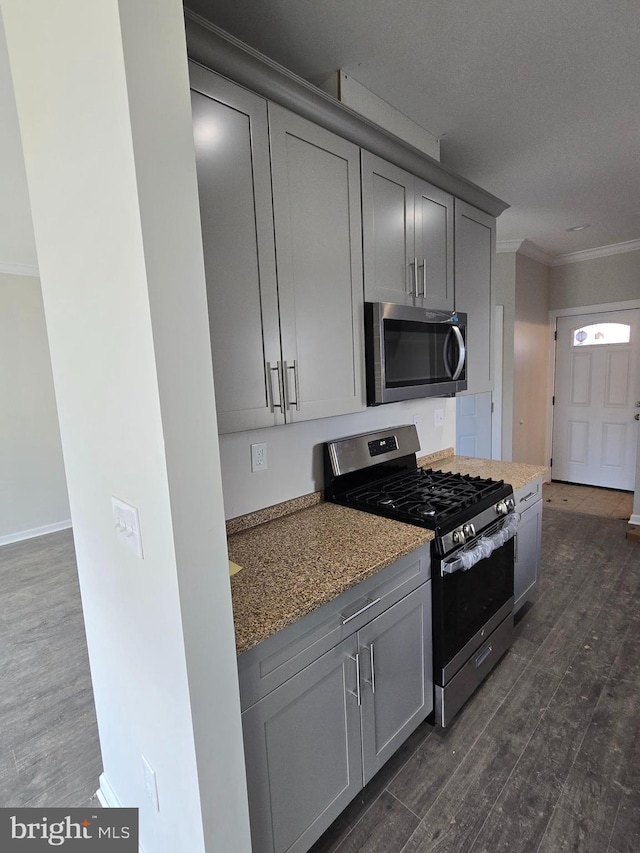 kitchen featuring stainless steel appliances, gray cabinets, dark wood finished floors, and crown molding