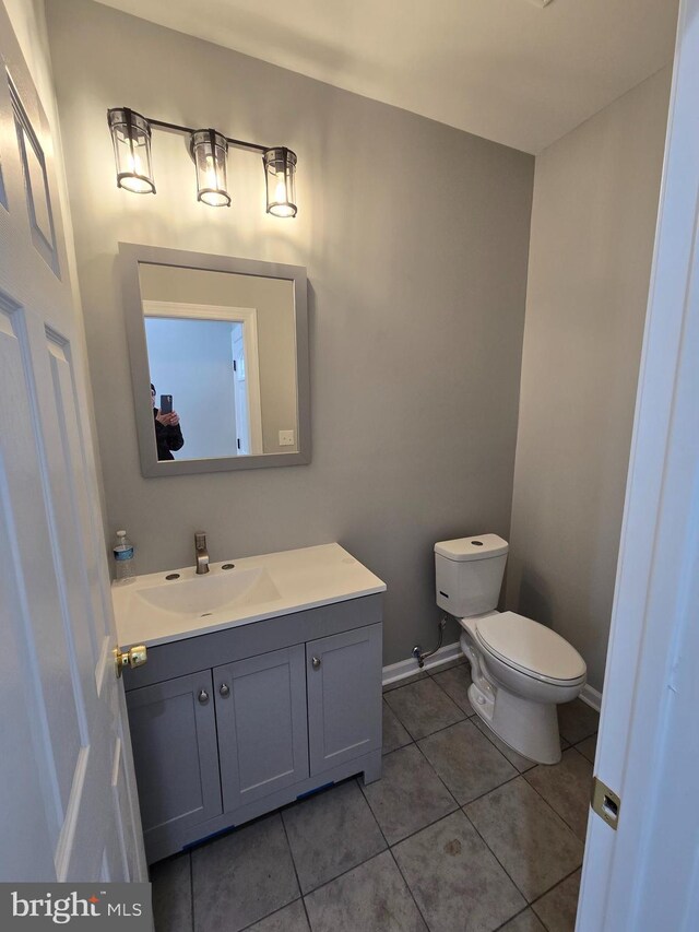 half bath with baseboards, vanity, toilet, and tile patterned floors