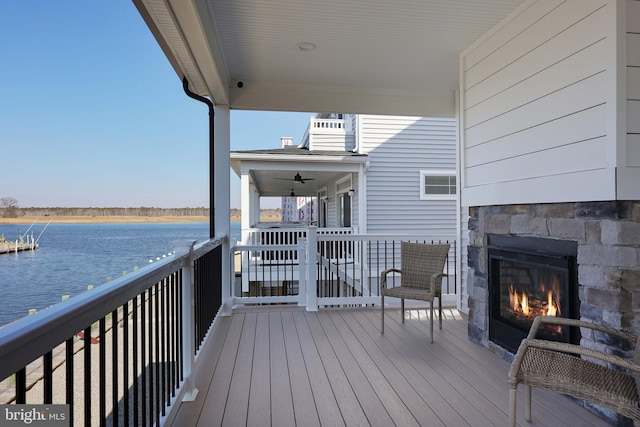 wooden terrace with an outdoor stone fireplace, ceiling fan, and a water view