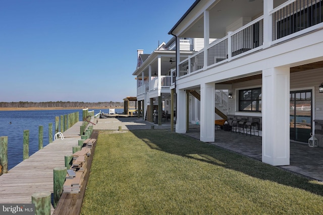 view of dock featuring a patio, a water view, and a lawn