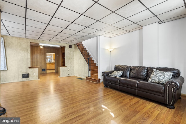 living room with hardwood / wood-style floors, a drop ceiling, and wood walls