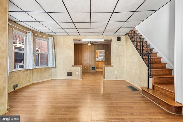 unfurnished living room with light wood-type flooring, ceiling fan, and wood walls