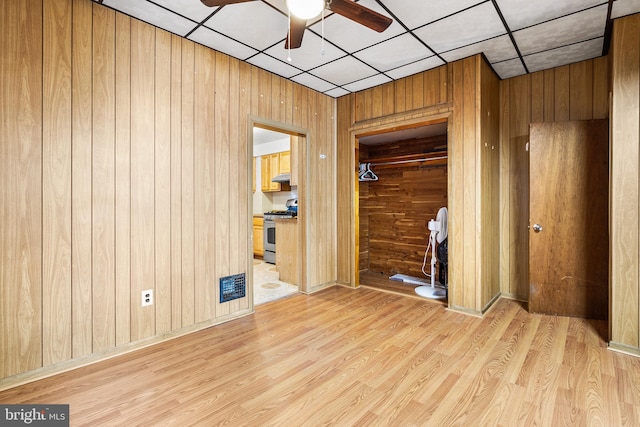 interior space featuring ceiling fan, a drop ceiling, wooden walls, and light hardwood / wood-style flooring