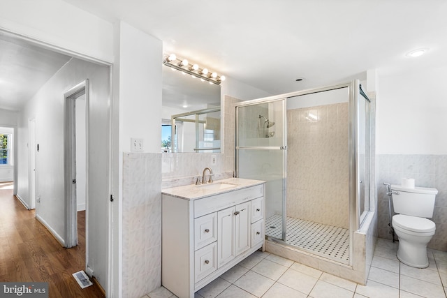 bathroom with tile patterned flooring, toilet, vanity, a shower with shower door, and tile walls