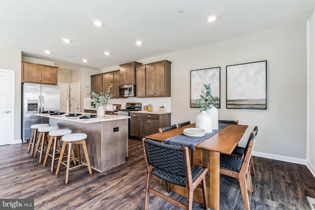 kitchen featuring a breakfast bar, stainless steel appliances, dark hardwood / wood-style floors, and a center island with sink