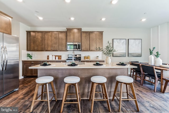 kitchen with a kitchen bar, stainless steel appliances, a kitchen island with sink, and dark wood-type flooring