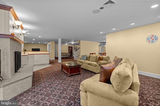 carpeted living room with a tiled fireplace, sink, and decorative columns