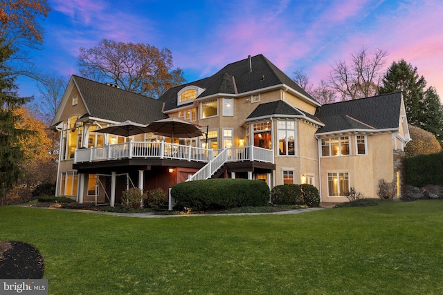 back house at dusk featuring a wooden deck and a lawn