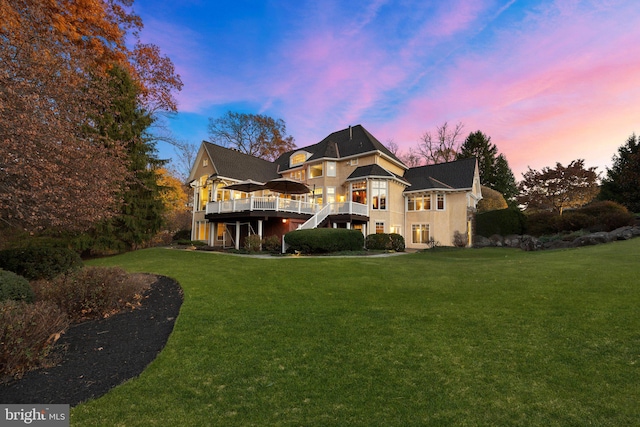 back house at dusk with a wooden deck and a lawn