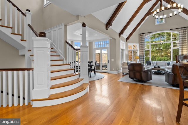 interior space featuring beam ceiling, high vaulted ceiling, a wealth of natural light, light hardwood / wood-style floors, and a chandelier