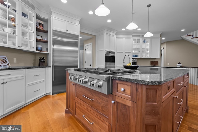 kitchen with white cabinetry, a center island, appliances with stainless steel finishes, pendant lighting, and dark stone counters