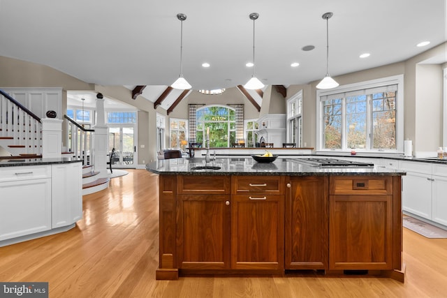 kitchen featuring pendant lighting, an island with sink, dark stone counters, stainless steel gas stovetop, and light wood-type flooring