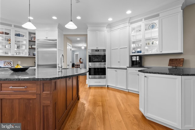 kitchen with white cabinetry, hanging light fixtures, a kitchen island with sink, and appliances with stainless steel finishes