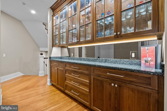 bar with light hardwood / wood-style flooring and dark stone countertops