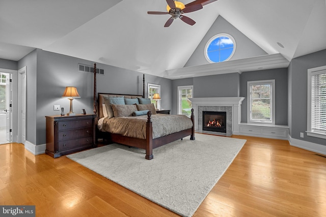 bedroom with hardwood / wood-style floors, a high end fireplace, high vaulted ceiling, and ceiling fan