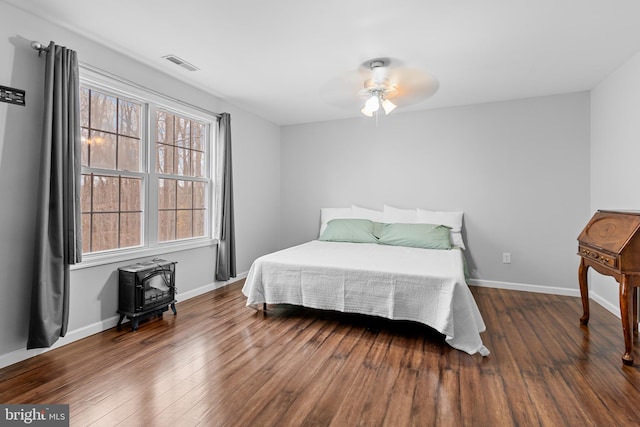 bedroom featuring ceiling fan, a wood stove, and dark wood-type flooring