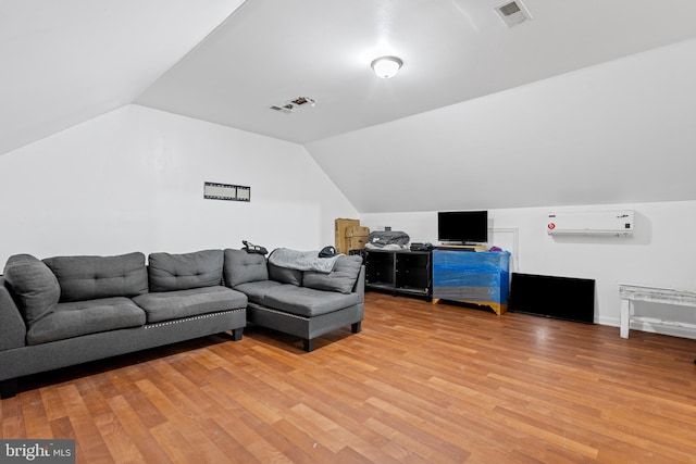 living room featuring a wall mounted AC, light hardwood / wood-style floors, and vaulted ceiling